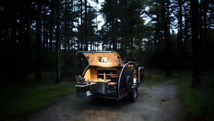 Minicaravana Caretta 1500 con la cocina abierta e iluminada al anochecer en el bosque