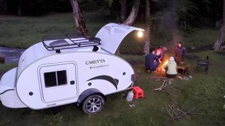 Viajar en familia en minicaravana. Jóvenes encendiendo una fogata junto a una minicaravana Caretta al atardecer