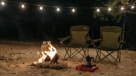 Fuego de acampada con dos sillas, cafetera y luces en una noche mágica en la naturaleza