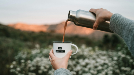 Persona sirviendo café de un termo en una taza durante un viaje en solitario en la naturaleza.