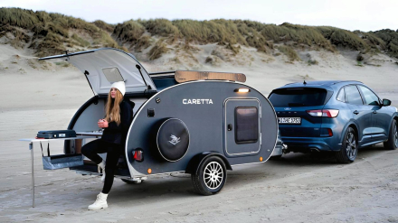 Chica joven con café disfrutando de un año sabático en minicaravana Caretta 1500 cerca de la playa en invierno