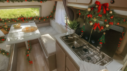 Interior de minicaravana Caretta Uncle decorada para Navidad, con mesa-comedor y cocina visibles