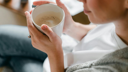 Mujer dentro de una caravana tomando una taza de café caliente para combatir el frío.